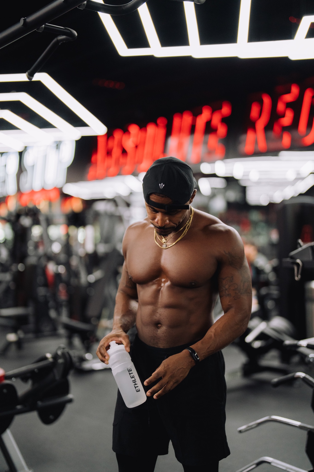 Alex Tellem holding an ETHLETE bottle under the gym neon