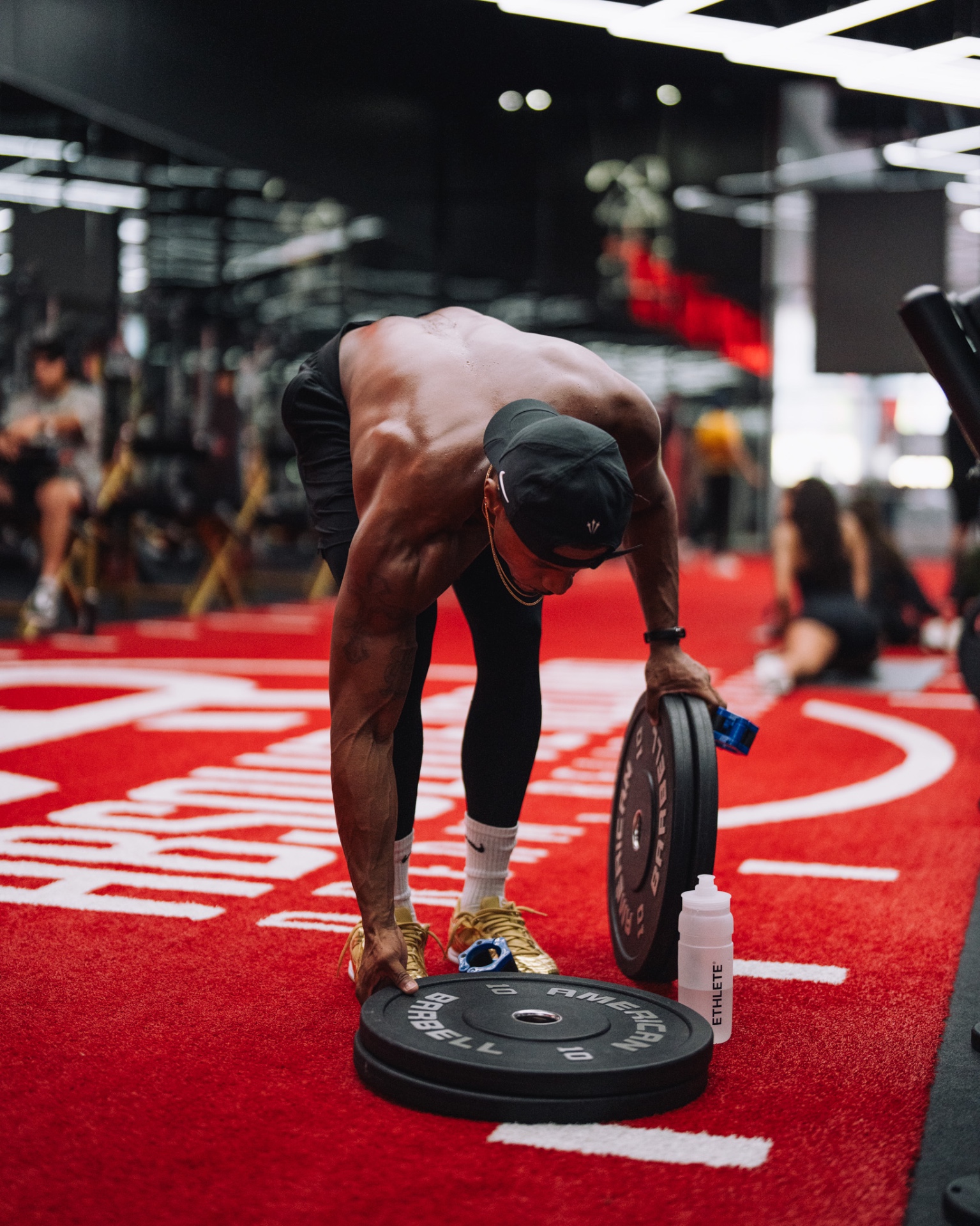 Alex Tellem loading plates with an ETHLETE bottle on the turf